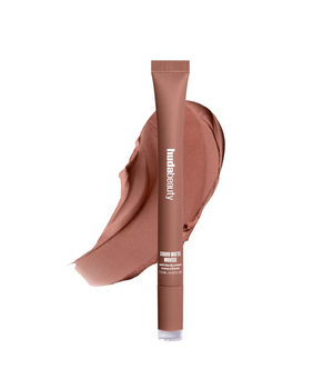 A tube of humateauty bronzer makeup in a warm medium brown shade, shown upright in front of a matching makeup smear on a plain white background.
