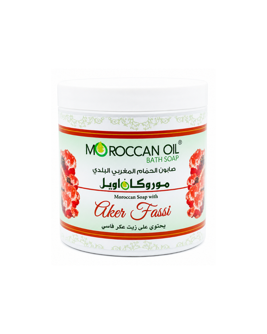 A white plastic jar of Moroccan Oil Bath Soap with a white label featuring red and green text and illustrations of red flowers, labeled 'Aker Fassi'.