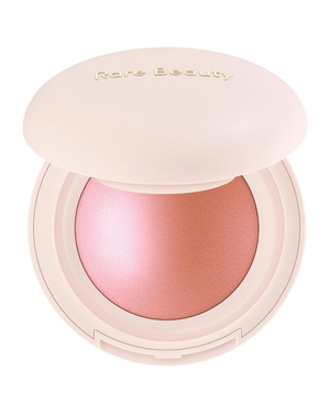 Rare Beauty blush compact in a pale pink case with the brand name embossed on the lid, showing a shimmering pink blush powder inside.